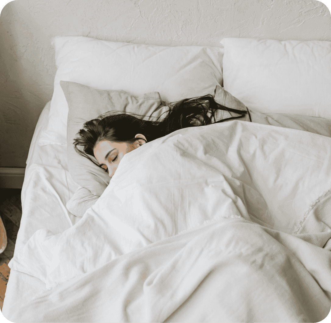 Vyhořelá žena ležící v posteli zakrytá peřinou.